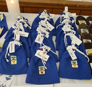 Acorn drawstring bags for youth, with cross-stitched heraldic devices, by THL Juanica Montanes, THL Delphine de Montallieu, Lady Faoiltighearna ni Dhuinn, Mistress Lynette de Sandoval del Valle de los Unicornios, Lord Ramvoldus Kröll, and Lady Kungund Benehonig.
