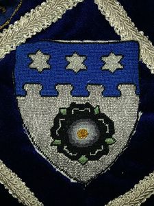 Aliskye Rosel Argent, a rose sable, barbed and seeded proper, on a chief nebuly azure three mullets of six points argent. (September of 1980 (via Caid). Maker: Aliskye Rosel.