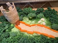 A wheat cracker tower stands at the end of a hummus pathway, surrounded by kale forest, broccoli bushes, and cauliflower sheep. Made for Dreiburgen Yule 2021