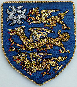 Éowyn Amberdrake Azure, in pale three dragons passant Or and for augmentation, in canton four crescents conjoined in saltire horns outward argent. (registered 7/04). Maker: Eowyn Amberdake Notes: The shield is silk dupioni, embroidered with typical Elizabethan stitches in gold and silver thread.