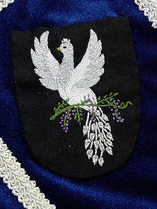 Cristobal degli Glicine che Mangia Uome Sable, a peacock rising, wings elevated and addorsed, maintaining a sprig of wisteria, all argent.(registered 08/88). Maker: Cristobal degli Glicine che Mangia Uome